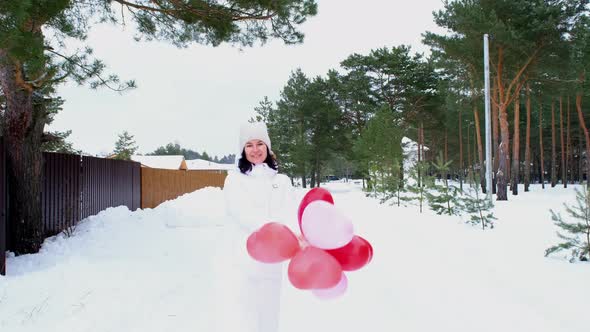 Happy woman throws up heart-shaped balloons outdoor in winter with snow alt