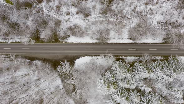 Winter country road with the view from above, fast driving cars passing by the straight street, top alt