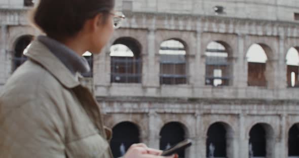 A Woman Dials a Message on Her Mobile Phone While Standing in Front of Coliseum alt