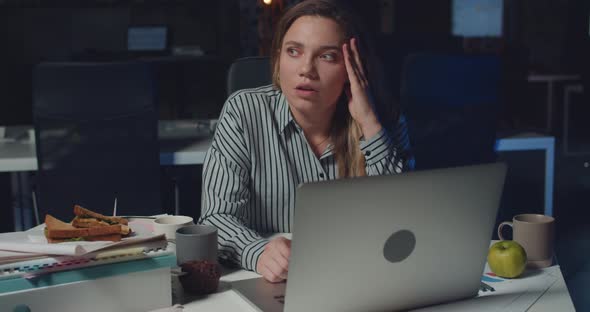 Front View of Tired Overworked Woman Sitting and Using Laptop Late in Office. Beautiful Girl Feeling