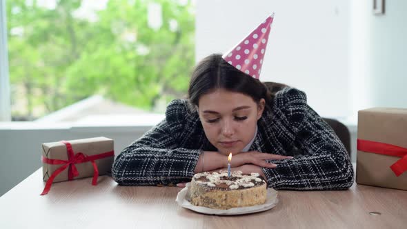 Sad Business Woman Celebrating Her Birthday Alone While Sitting in the Office Blows Out the Candle alt