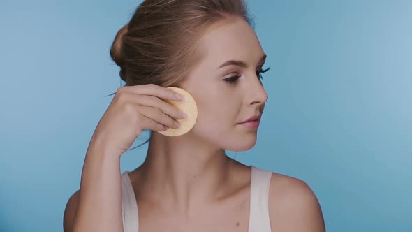 Woman Cleansing Face with Two Sponges and Turning To Side alt