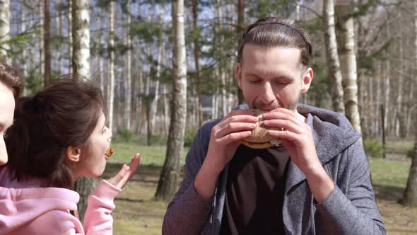 Man and a Woman Talk and Joke at a Dining Table in Nature and Eat a Burger