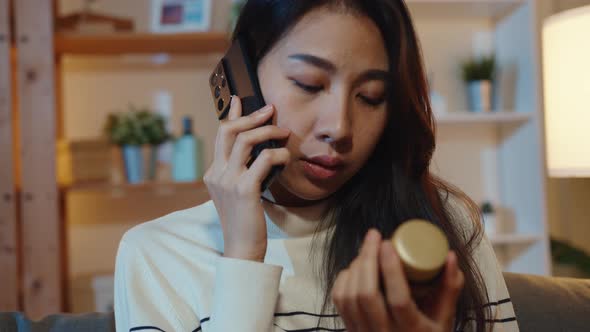 Sick young Asian lady hold medicine sit on couch video call with phone consult with doctor at home