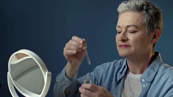 Beautiful Elderly Woman Applies a Moisturizing and Nourishing Cosmetic Product for Skin Care alt