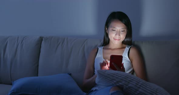 Woman use of smart phone and sit on sofa at home in the evening alt