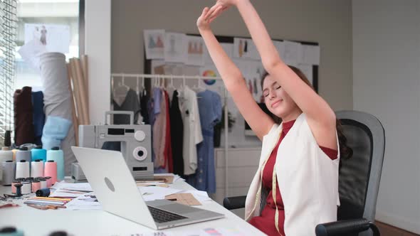 Young professional designer or tailor sit on chair and do stretch lazily during work with laptop