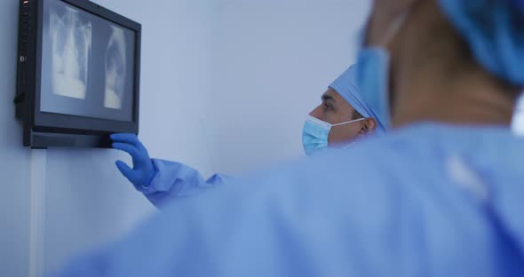 Mixed race male surgeon wearing protective clothing presenting x-ray on screen alt