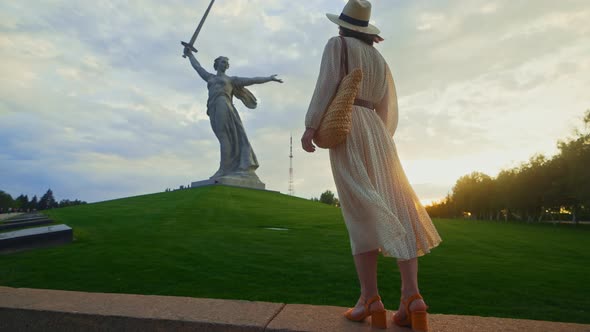 A young girl looking at Mother Motherland on the Mamayev Kurgan at sunset alt
