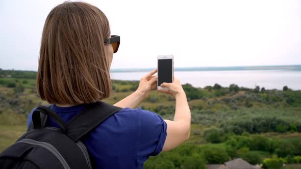 Caucasian Woman with Backpack Filming Green Landscape Around Her