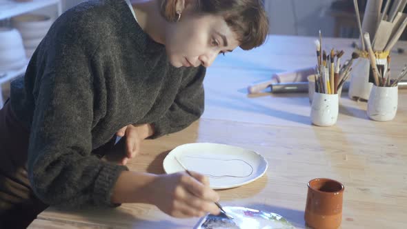 Artist woman working with ceramic plate in the art workshop