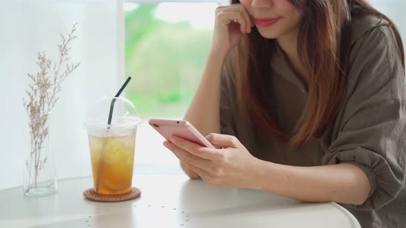 Young woman with drinks using mobile phone and relaxing in cafe