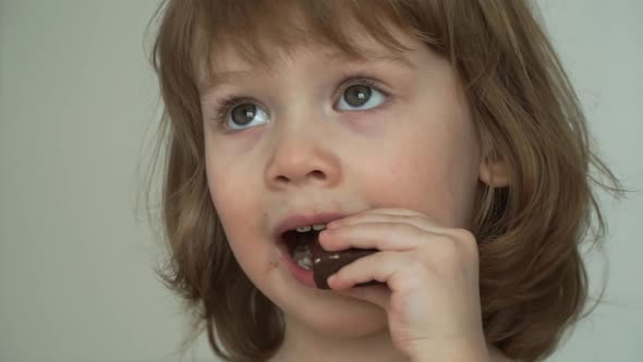 Close Up of Little Soiled Funny 3 Year Old Girl Eats with Big Appetite Piece of Tasty Chocolate
