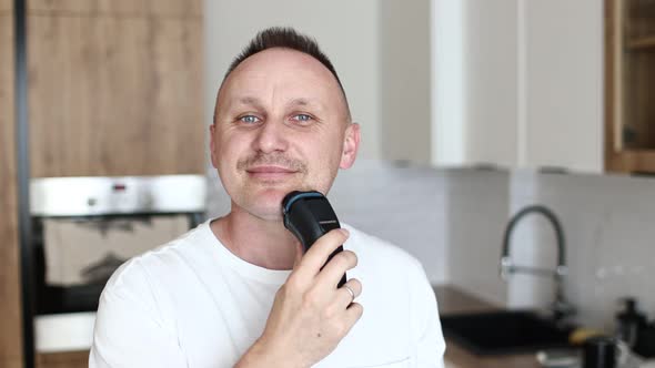 funny handsome caucasian man guy male in white t shirt shaving with electric razor having fun shavin