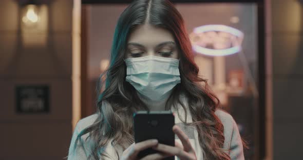 Young woman in the city street wearing a surgical mask and connecting with her smartphone