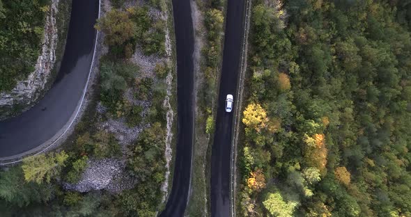 Aerial Top Down White Car Driving Down an Asphalt Road Crossing the Mountiain