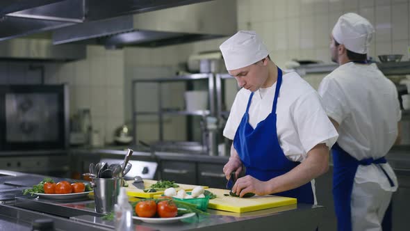 Caucasian Cook Slicing Cucumber Eating Slice As Chef Passing at Background alt