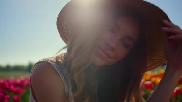 Beautiful Woman Portrait Taking Off Straw Hat in Sunlight in Floral Background alt