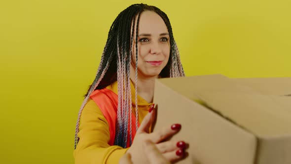 Young Woman in Vest with Cardboard Box on Yellow Background in Studio alt