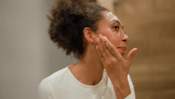 African woman washing with facial foam in the bathroom alt