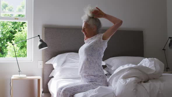 Senior caucasian woman stretching her arms while sitting on the bed at home alt