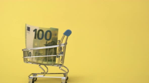 Shopping Cart with One Hundred Euro Banknote on Yellow Background Buying Currency