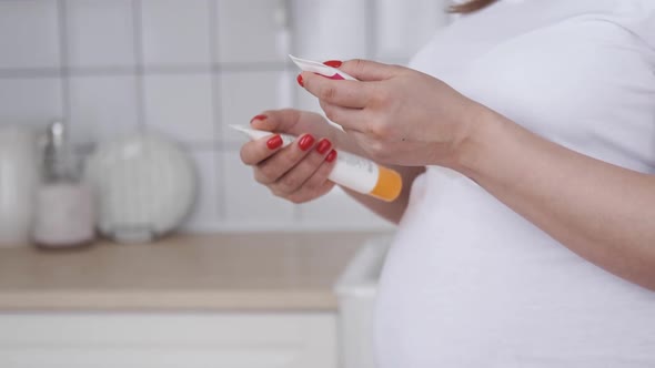 Pregnant Woman Hands with Smartphone Reading Label on a Bottle alt