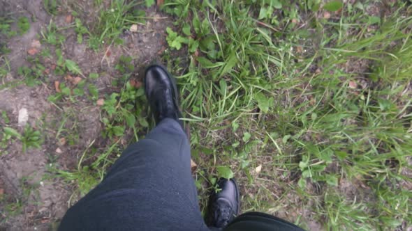 Human Feet in Black Shoes Walk on the Ground and Grass