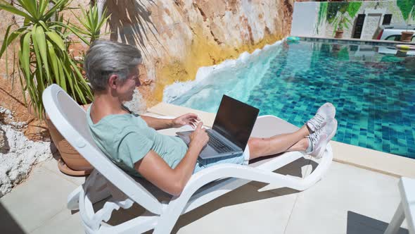Side View Man Lying By the Pool and Working on Laptop Computer with White Blank Screen Male Hands alt