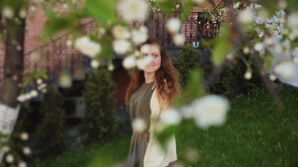 Beautiful Young Woman Stands Under a Blooming Apple Tree in a Spring Garden