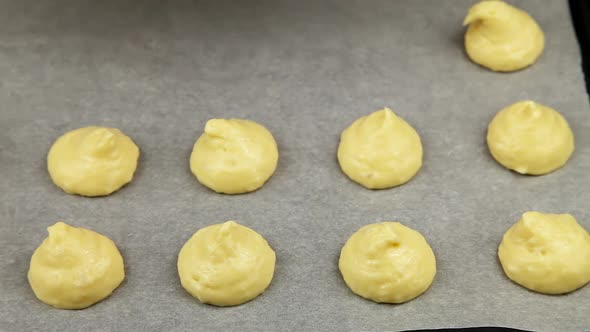 The pastry chef squeezes profiterols onto parchment paper with a baking bag.