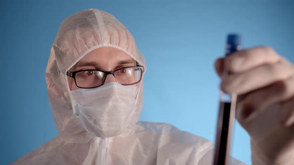 Man in Protective Suit Medical Mask Gloves Holds Test Tube with Coronovirus