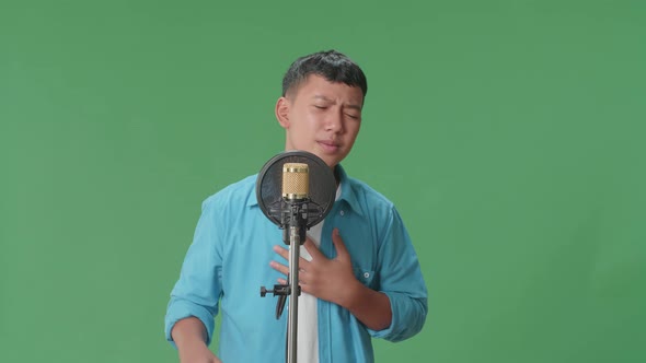 Young Asian Boy Singing Into Microphone In Green Screen Studio alt