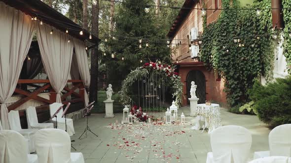 Wedding Arch with Red Flowers and White Chairs Lamp Garland Over the Ceremony Near Restaurant Slow alt