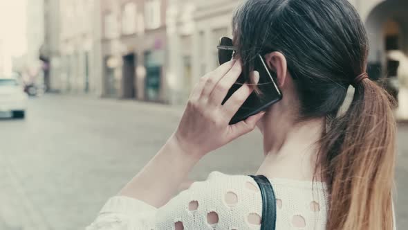 An adult woman is talking on a mobile phone while standing on the street.