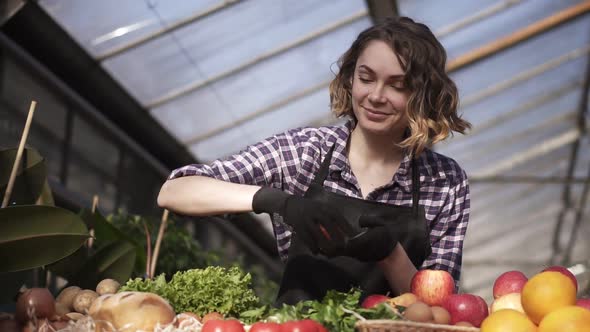 Low Angle View of a Beautiful Smiling Woman Farmer in Black Gloves Arranging Organic Food in Farm alt