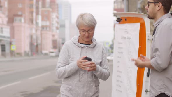 Senior Mixed Race Lady Buying Coffee from Street Van and Drinking alt