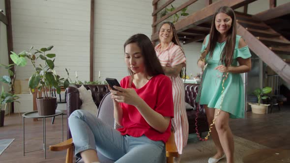Young Woman Browsing Smartphone Against Background of Dancing Friends alt