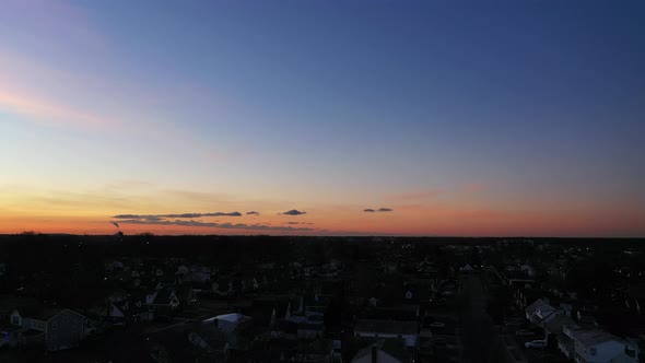 An aerial shot over a suburban neighborhood at sunrise. The camera dolly in towards the horizon whil alt