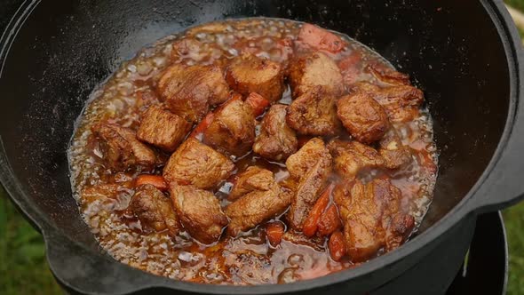 Cooking Process, Frying Pork Meat With Carrots and Onion in Large Cauldron on Open Fire.