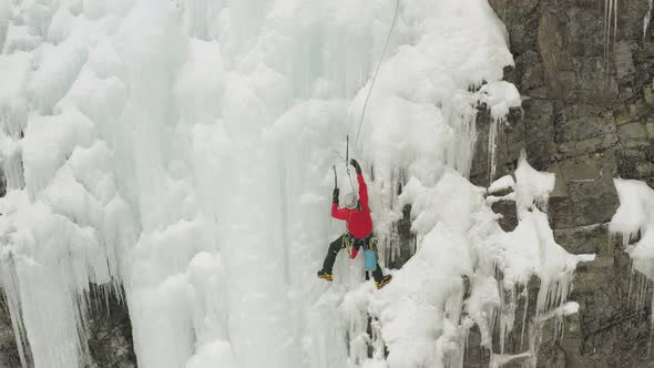 Single climber on frozen ice cascade preparing safety line 4K alt