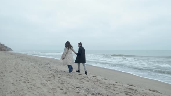 Happy Couple Walking on the Wild Beach on Cloudy Sunrise or Sunset alt