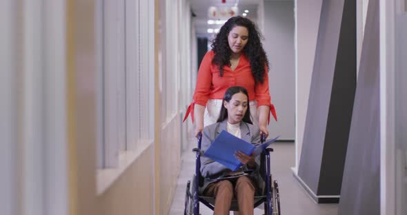 Happy biracial businesswoman with disabled colleague in wheelchair working together in modern office alt