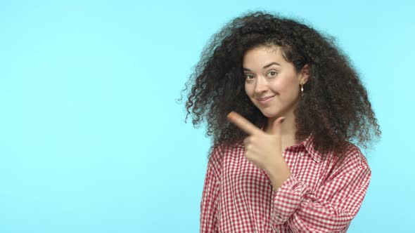 Slow Motion of Trendy Girl with Dark Curly Hair Pointing Finger Left Nod and Recommend Product