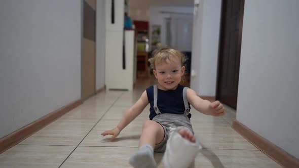 Happy Cute Toddler After an Accidental Fracture of His Leg Moves Around the Apartment with a Plaster alt
