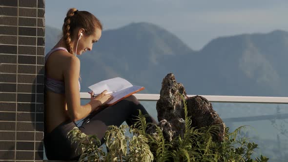 Girl Scrolls Through Pages Making Notes on Roof alt
