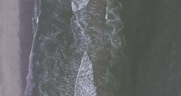 A topdown drone shot by the sea, during sunset, panning back and waves rolling in alt