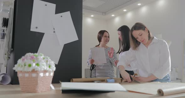 Three Fashion Designer Works at a Table and Discuss About Something Curves and a Pattern Scissors alt
