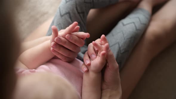 Mom's hands caress the hands of her little daughter, top view alt