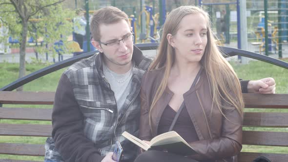 Married Couple Sitting on Bench in the Park in the Spring and Reading an Interesting Book alt